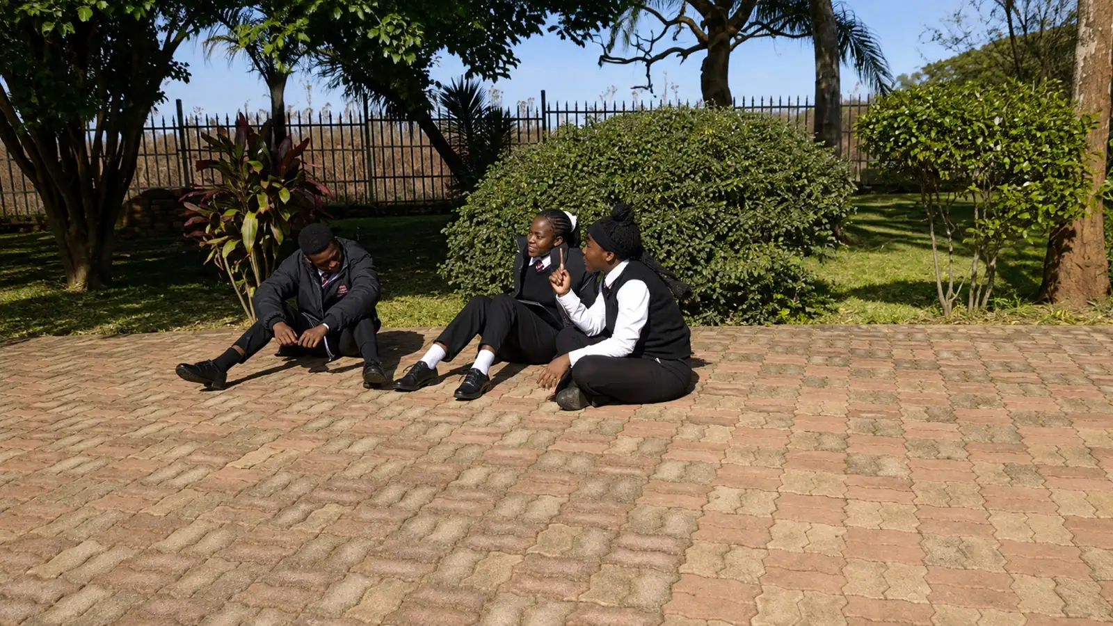 Three Privian Academy pupils sitting together on the paving in the school grounds